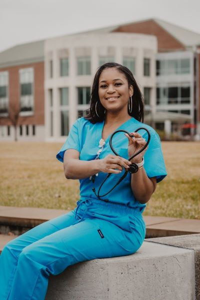 A Black female healthcare professional holds her stethoscope in the shape of a heart